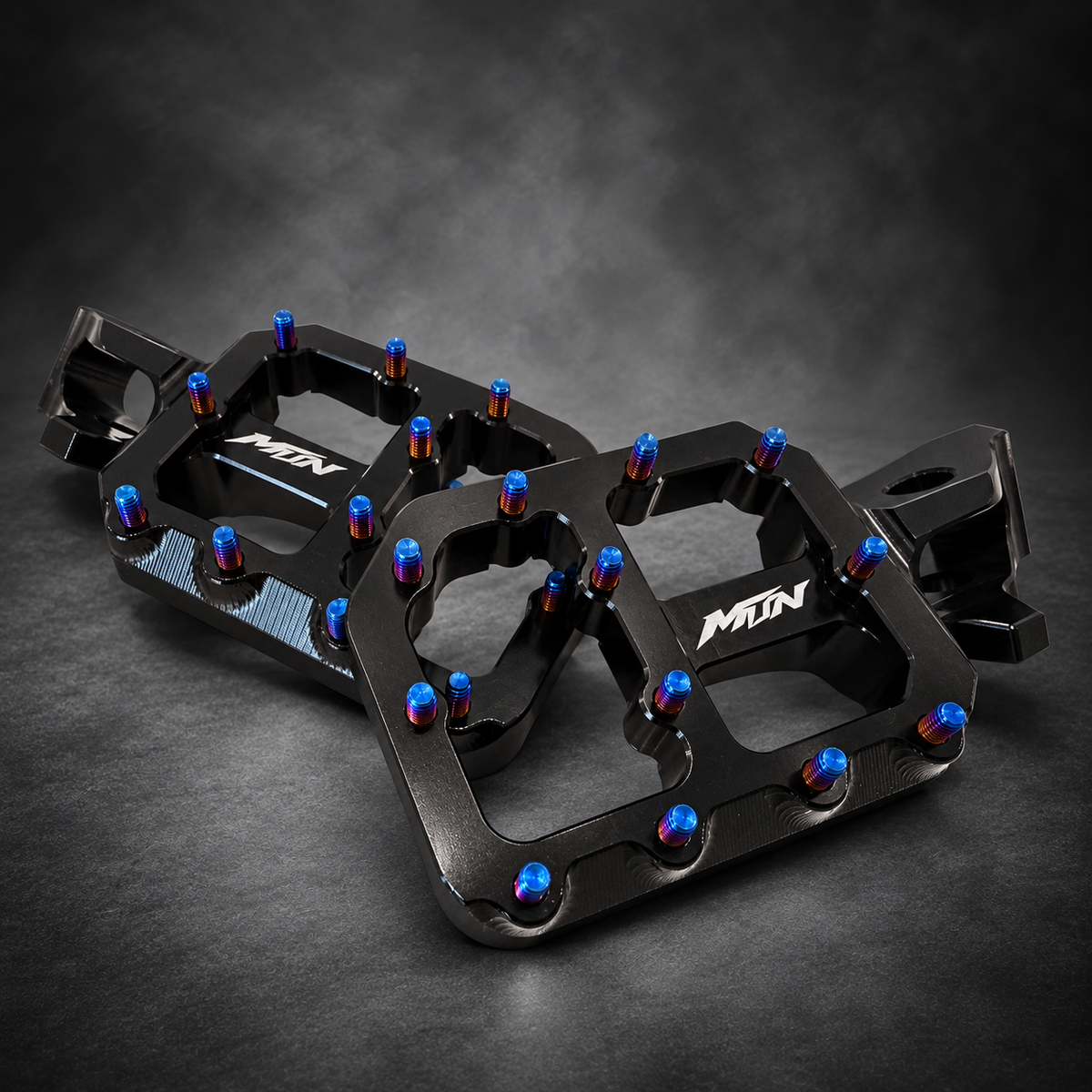 MTN MARK II Black Ultra Bee footpeg pair showing CNC machining and Titanium Blue pins
