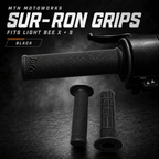 Black Sur-Ron rubber handlebar grips for Light Bee X and S, shown installed on the bar with a spare pair